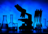 Rescheduling Cannabis: The Coming Collision with Ag-Biotech Regulation Silhouetted laboratory microscope, glass beakers, test tubes, pipettes, and sample bottles against a blue background for a cannabis biotechnology research story.