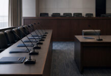 Who Will Argue Against Cannabis Rescheduling at DEA’s June Hearing? An administrative hearing room with seven microphones arranged at one counsel table and a single microphone across the room.