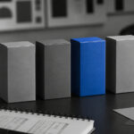 Cannabis Brands Need More Than Legacy, Passion, and Quality A vivid blue product box stands out among several gray boxes on a monochrome branding workspace.