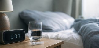 Saliva collection tube beside a clock and water glass in early morning light