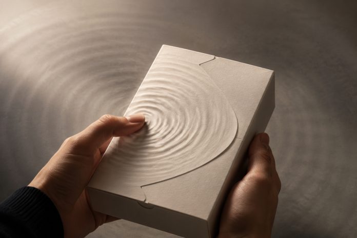 packaging first product experience Hands hold an unbranded textured package as ripples radiate from a fingertip.